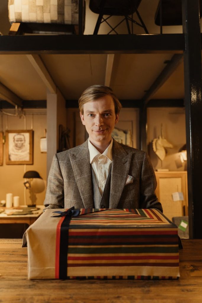 A man in business attire inside a vintage store with a wrapped gift box on display.