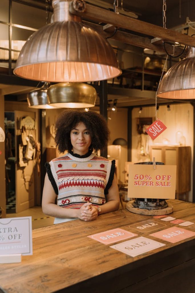 Fashionable store setting with afro-textured hair model showcasing sale signs on a wooden table.